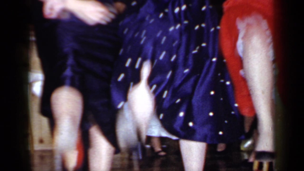 Dancers in dark and patterned dresses move closely together with legs and skirts visible.