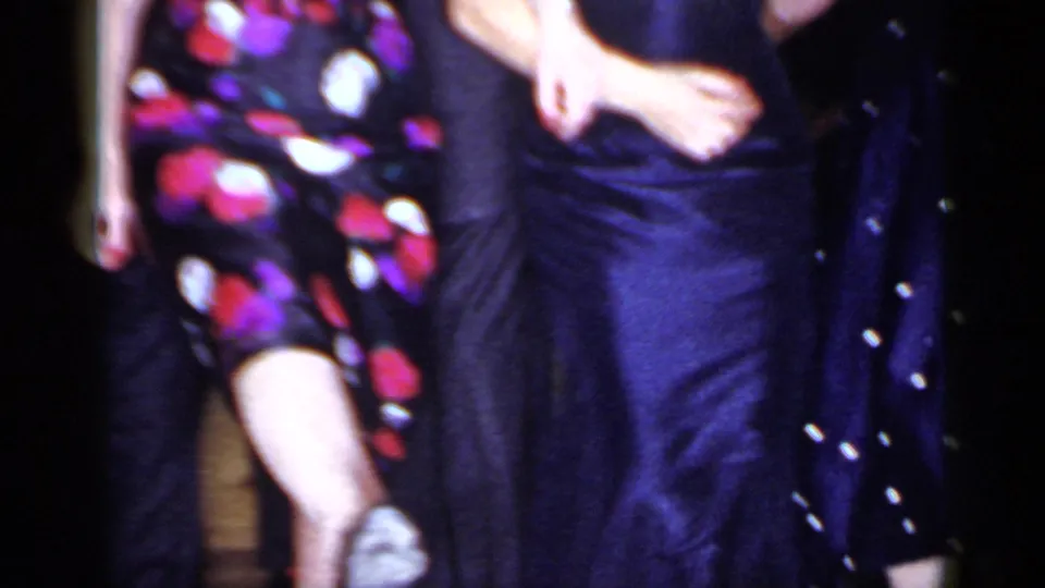 Close 8mm frame from the Mineola dance party with a floral-patterned dress, dark suit, and moving legs filling the view.