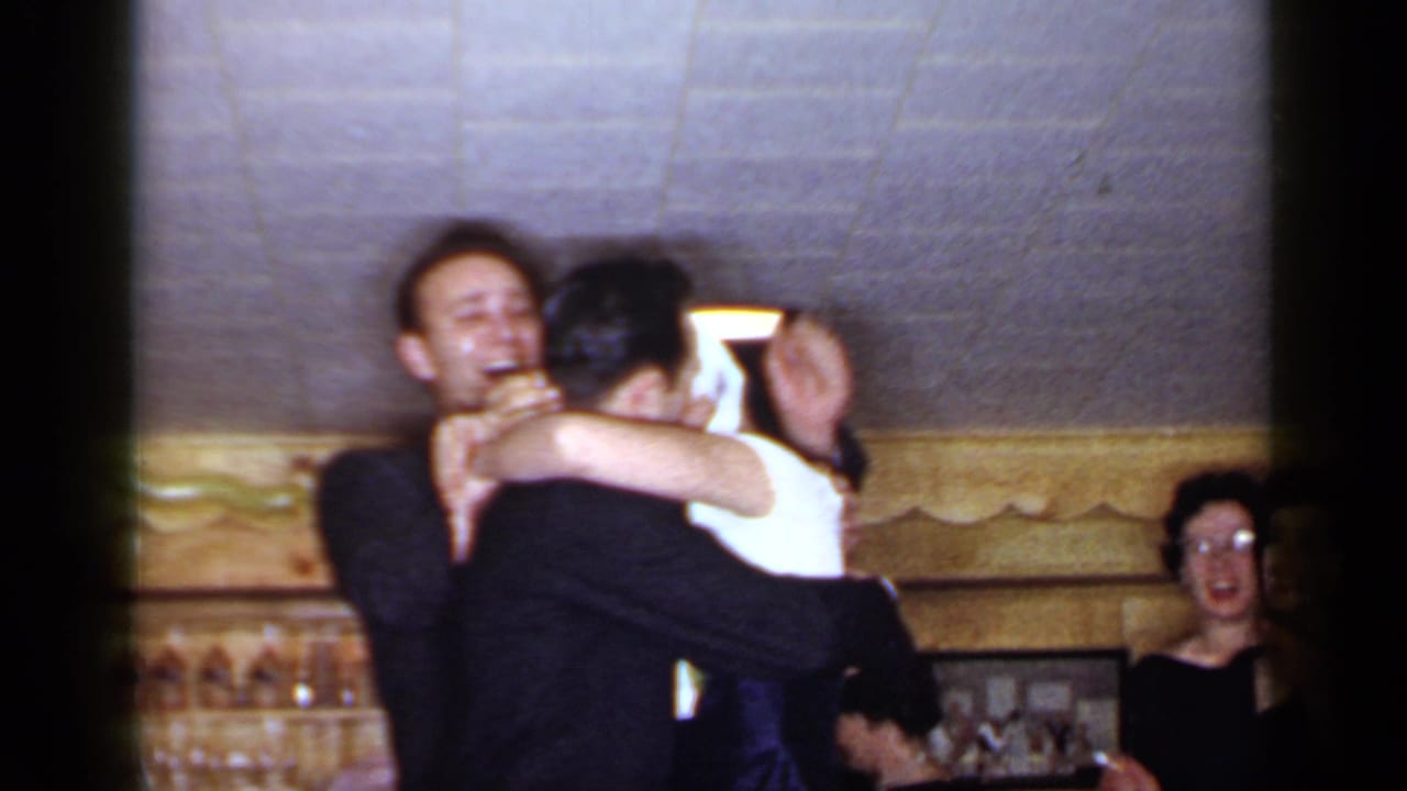1966 Mineola reception footage shows a laughing man holding a blindfolded woman in a white dress with guests in the background.