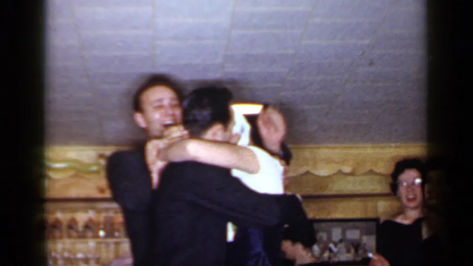 1966 Mineola reception footage shows a laughing man holding a blindfolded woman in a white dress with guests in the background.