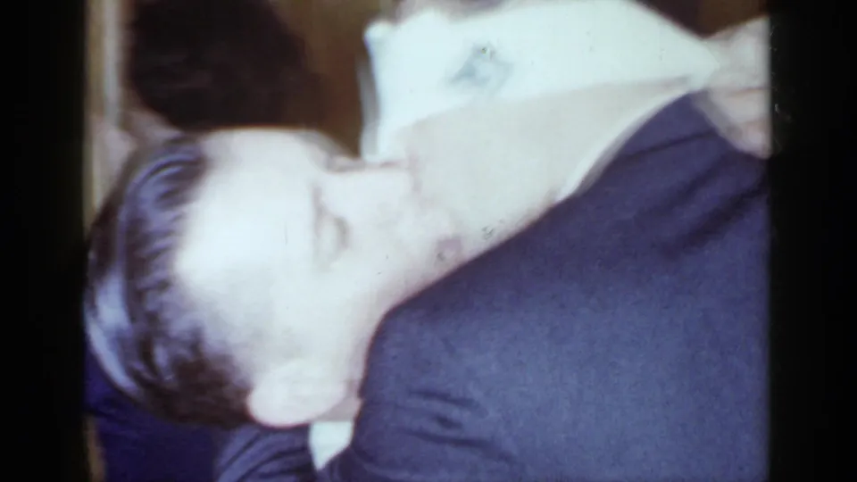 Close 1966 Mineola party frame with two adults leaning into a playful kiss or embrace during the blindfold game.