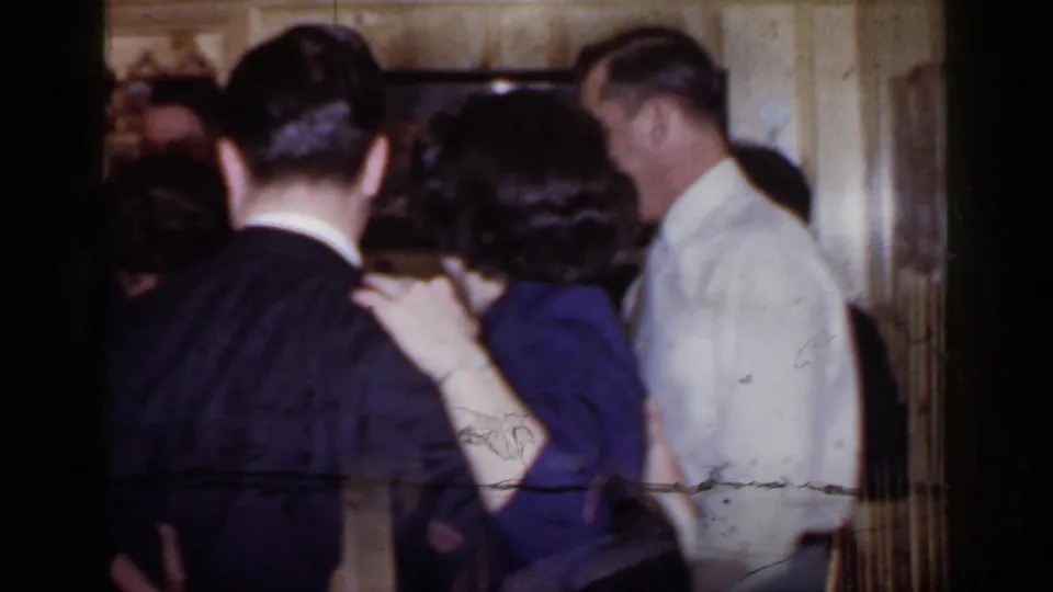 1966 Mineola, New York home-movie frame showing adults dancing closely in a wood-paneled interior during a party.