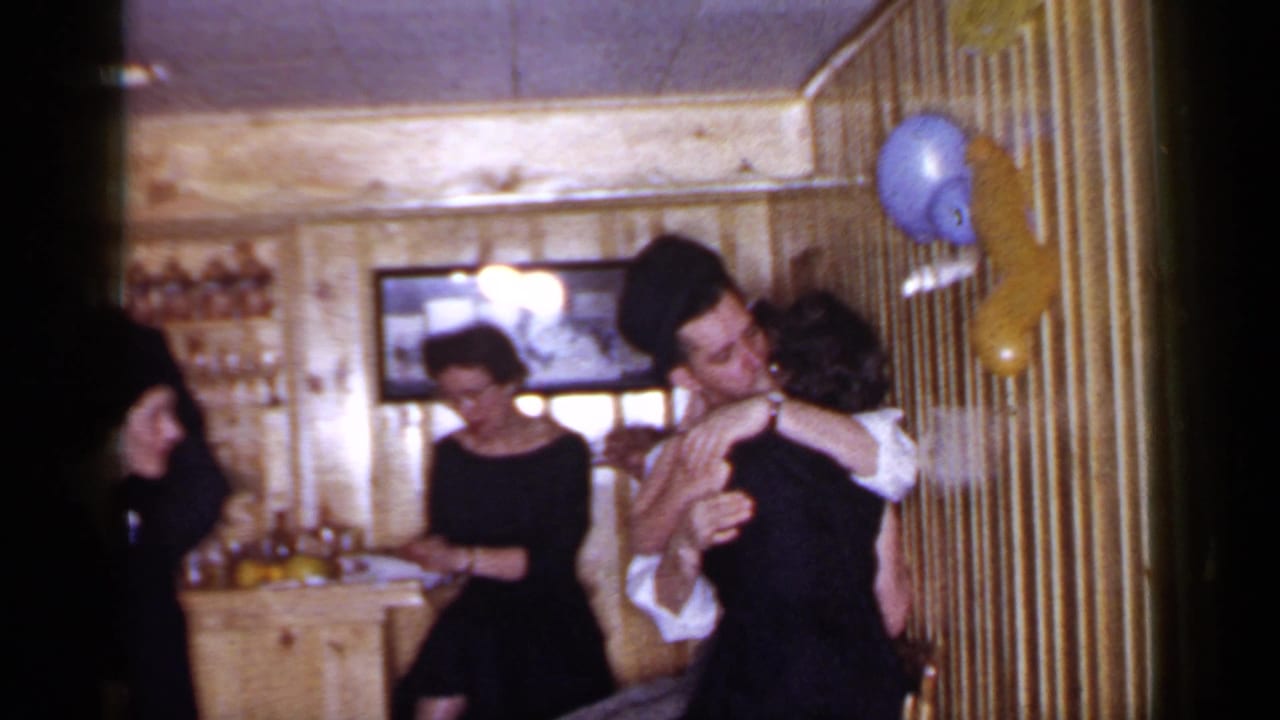 1966 Mineola party frame with a couple embracing and kissing beside balloons as guests mingle near a bar.