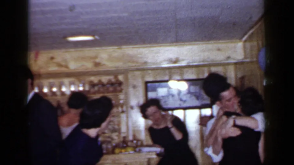 1966 Mineola party frame with guests mingling near a bar and a couple kissing along the wood-paneled wall.