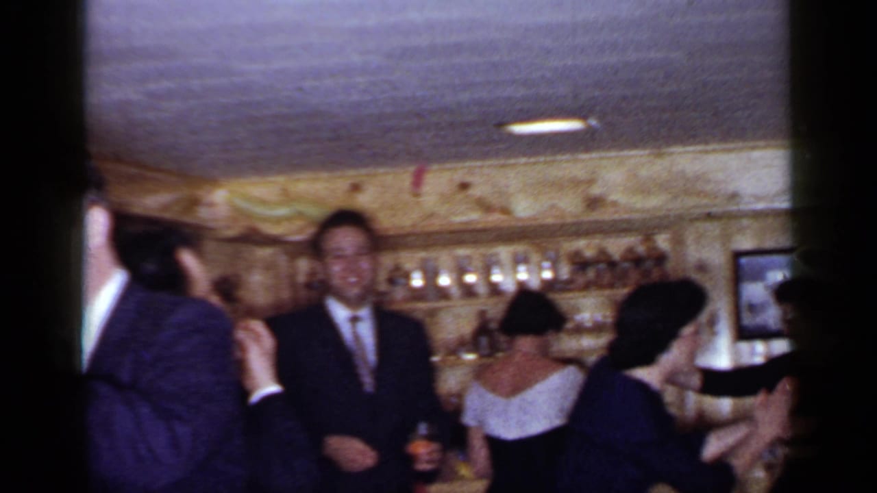 Adults in suits and dresses stand near bar shelves, with several guests dancing or holding drinks.