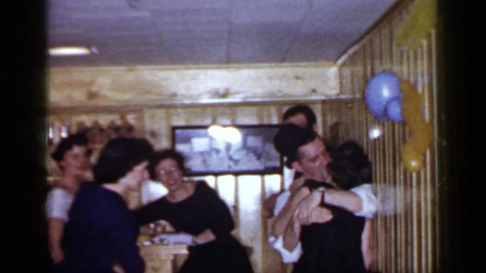 1966 Mineola reunion frame with laughing adults near the bar and a couple embracing beside blue and yellow balloons.