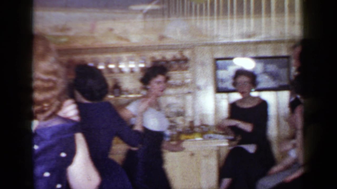 Adults gather near a bar area with glassware while one guest holds a balloon.