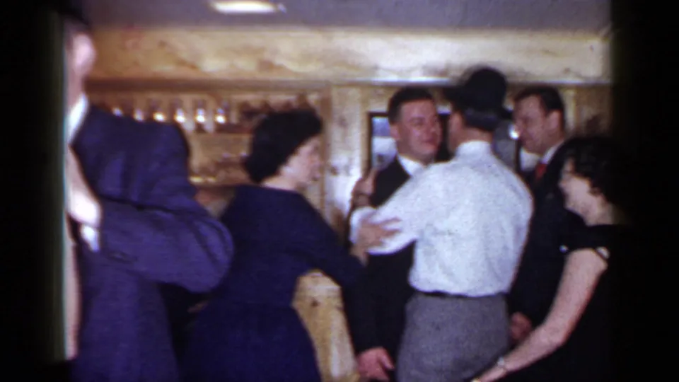 Adults in suits and dark dresses dance together in a crowded private interior in the 1966 Mineola home-movie clip.