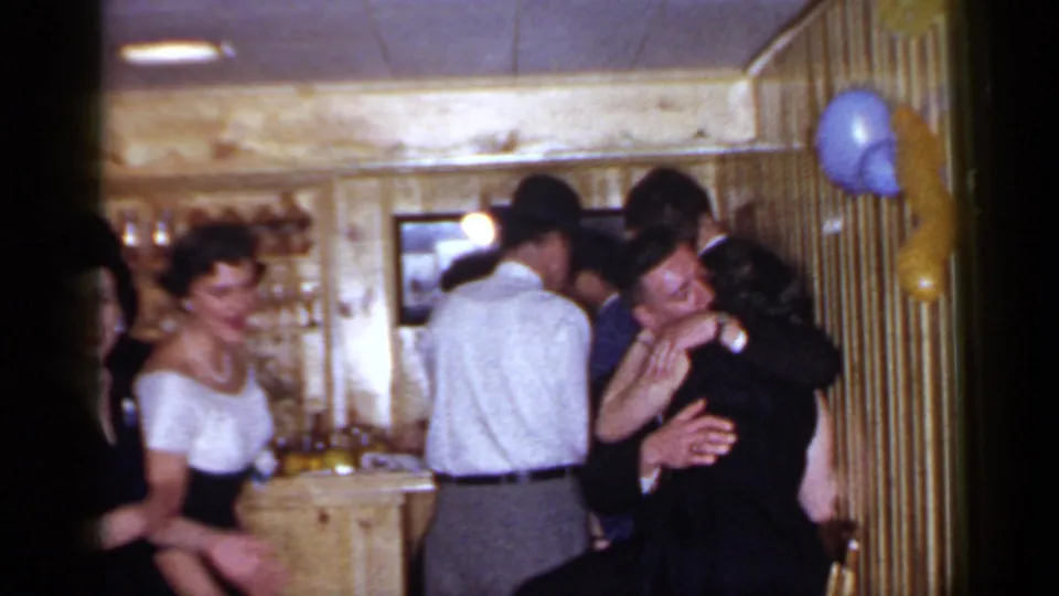 1966 Mineola party frame with adults in 1960s attire gathered by a wooden bar, balloons on the wall, and an embracing couple at right.