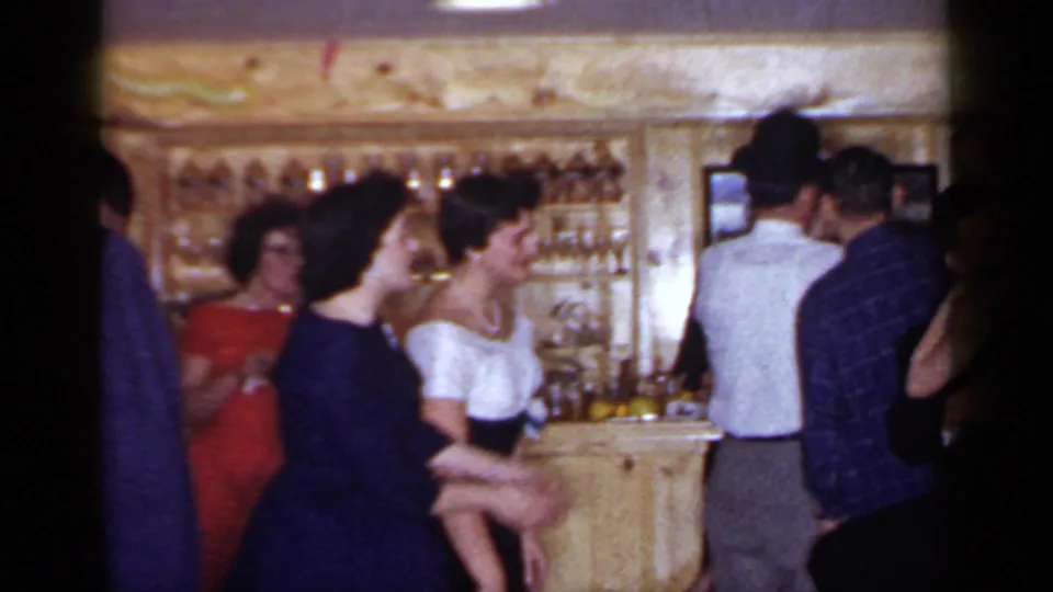 1966 Mineola party frame with smiling women and men gathered in a wood-paneled bar, with liquor shelves and balloons visible behind them.