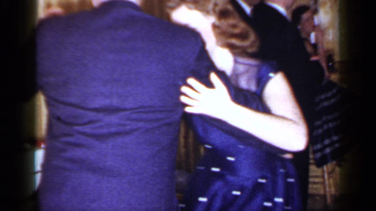 The couple turns while dancing, with other formally dressed guests visible behind them.