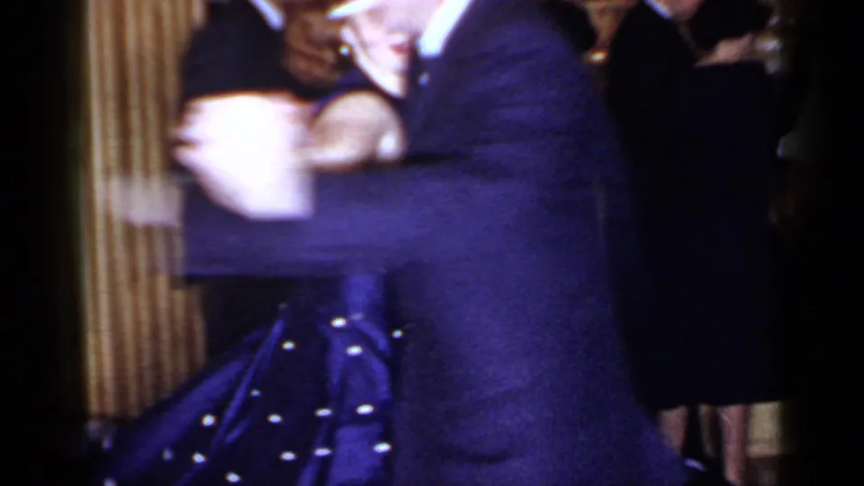 Motion-blurred 8mm frame of the couple dancing closely at the 1966 Mineola indoor social event.
