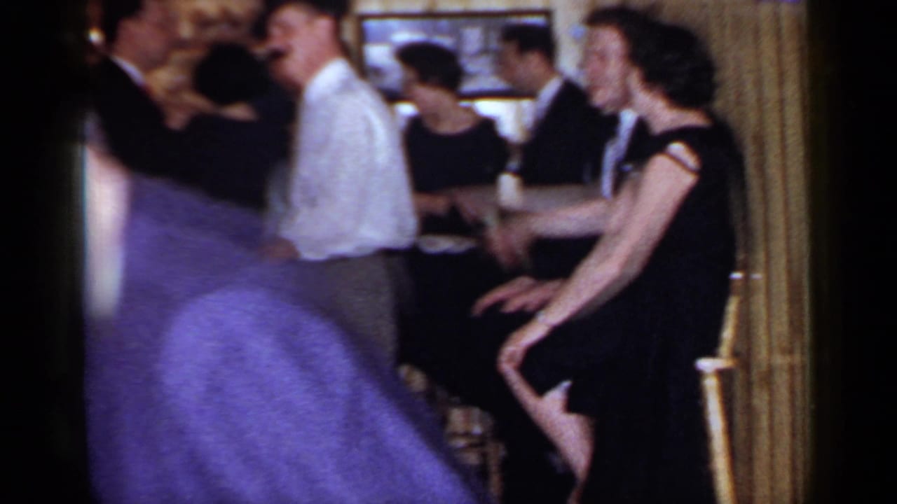 1966 Mineola home-movie frame with adults in suits and dresses dancing and mingling inside a private room.