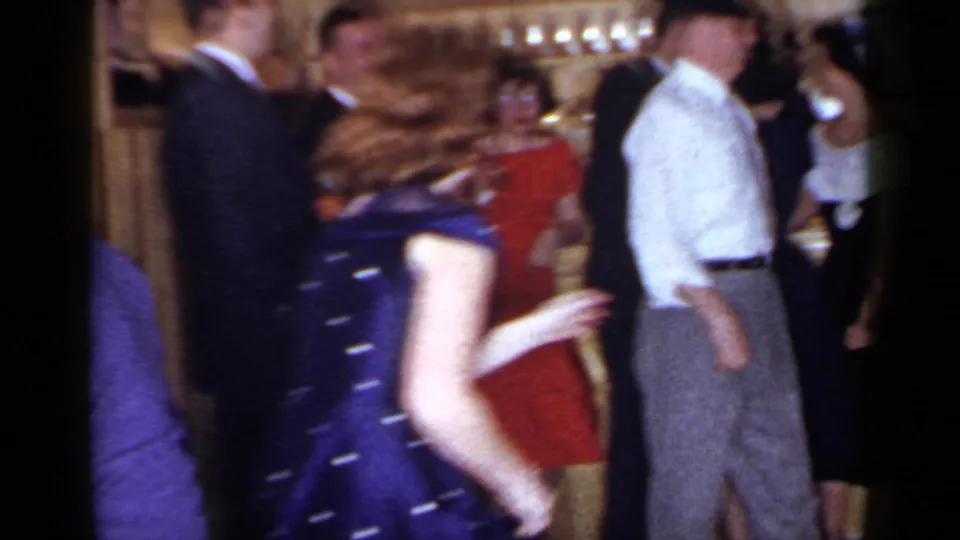 1966 Mineola home-movie frame showing guests dancing indoors, including a blue polka-dot dress and a man in a white shirt.