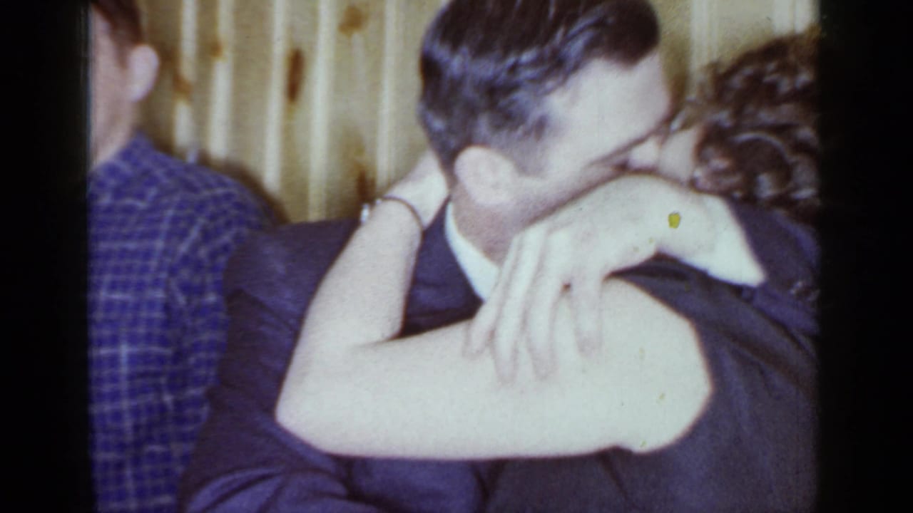 1966 Mineola party frame with an adult couple embracing and kissing while other guests stand nearby.