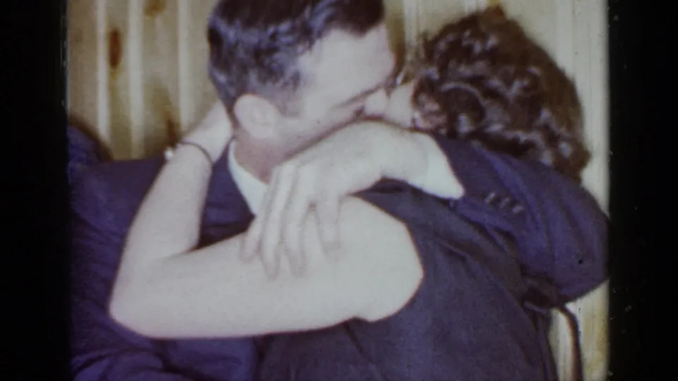 Close 1966 home-movie frame of a couple kissing at a private indoor party in Mineola, New York.