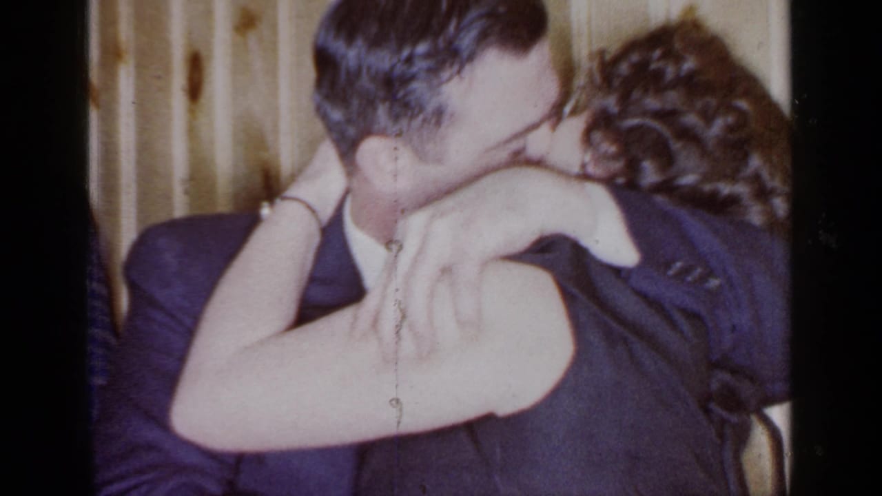 Man and woman kiss closely in a crowded indoor party setting.