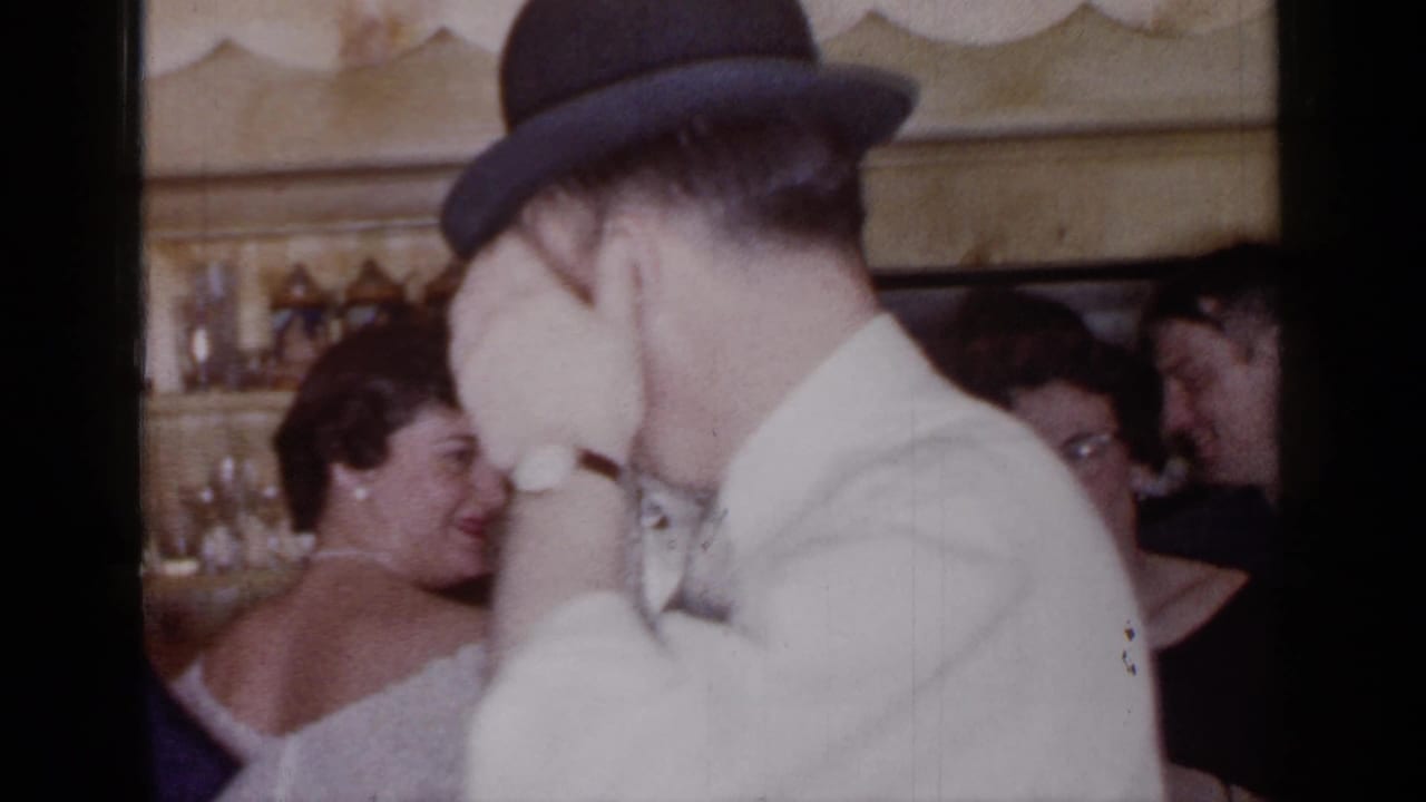 Man in a bowler hat dances or turns near women in evening dress.