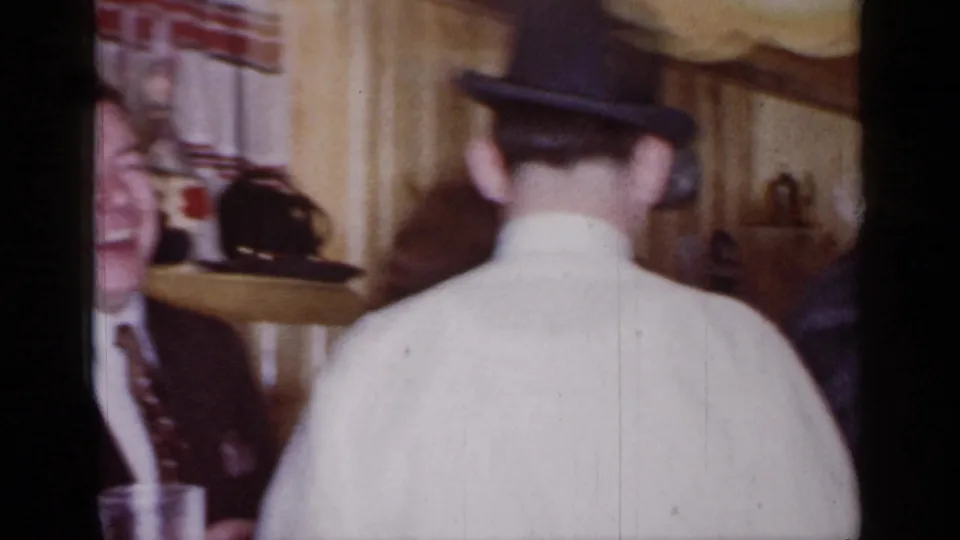 A man in a dark hat and white shirt is seen from behind in the 1966 Mineola party interior.