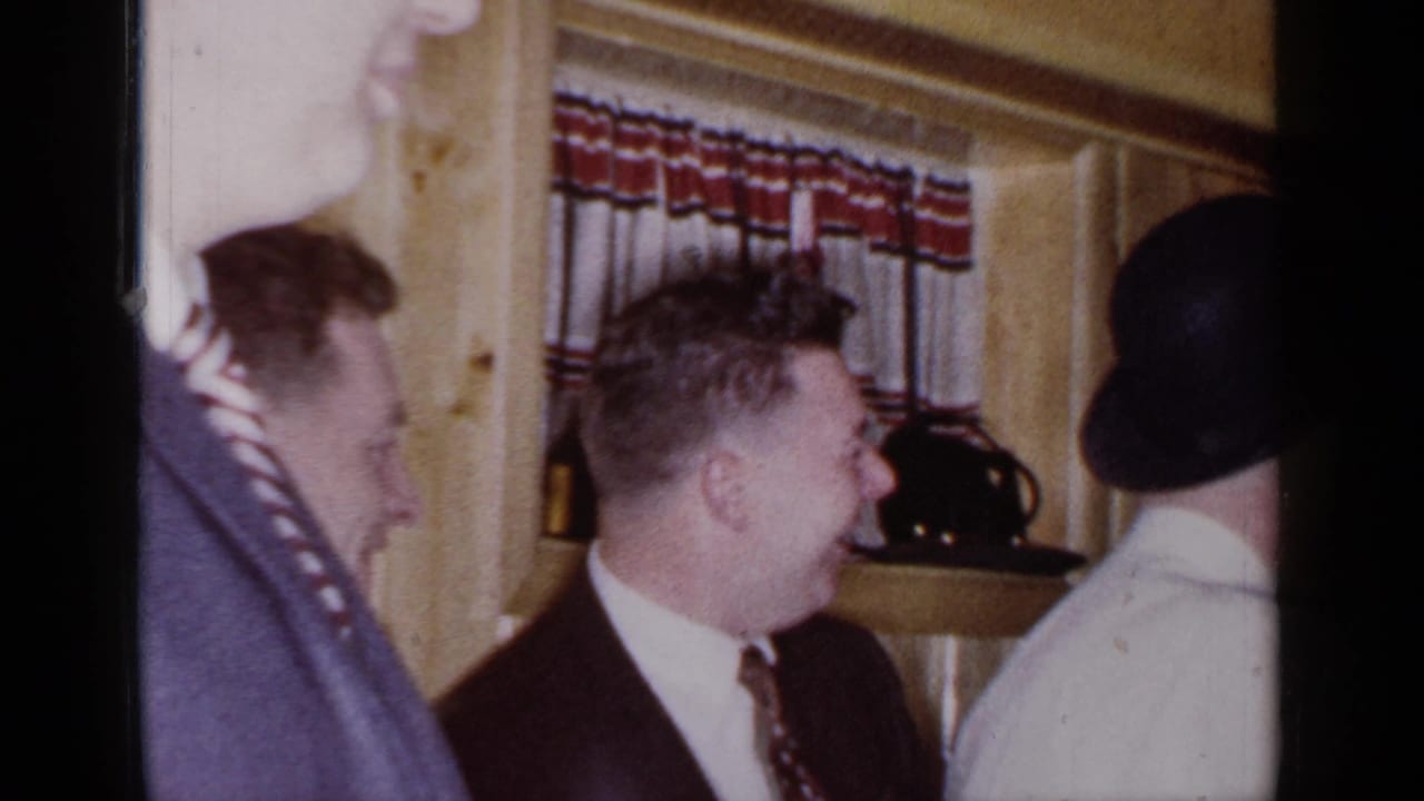 Well-dressed adults stand in a wood-paneled room near patterned curtains.