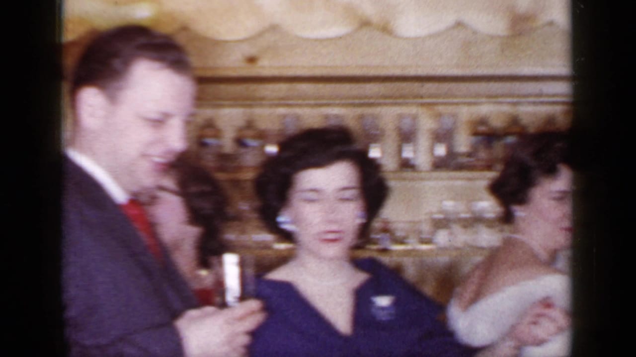 Adults in formal clothes stand close together, with one man holding a drink.