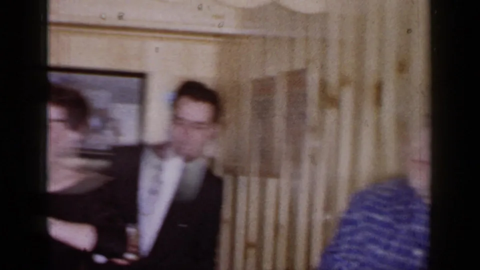 Handheld 1966 home-movie frame shows blurred adults moving during an indoor gathering in Mineola, New York.