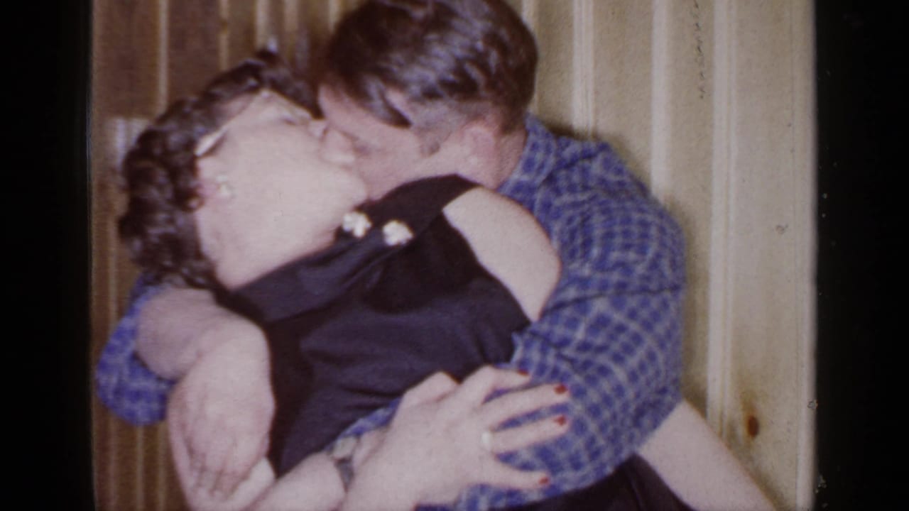 Couple kissing closely, with the man holding the woman near a paneled wall.