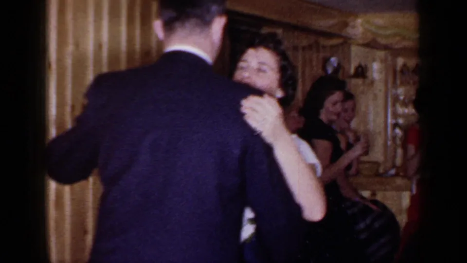 A suited man dances with a woman in a 1966 Mineola bar or party room, with guests visible near the counter behind them.
