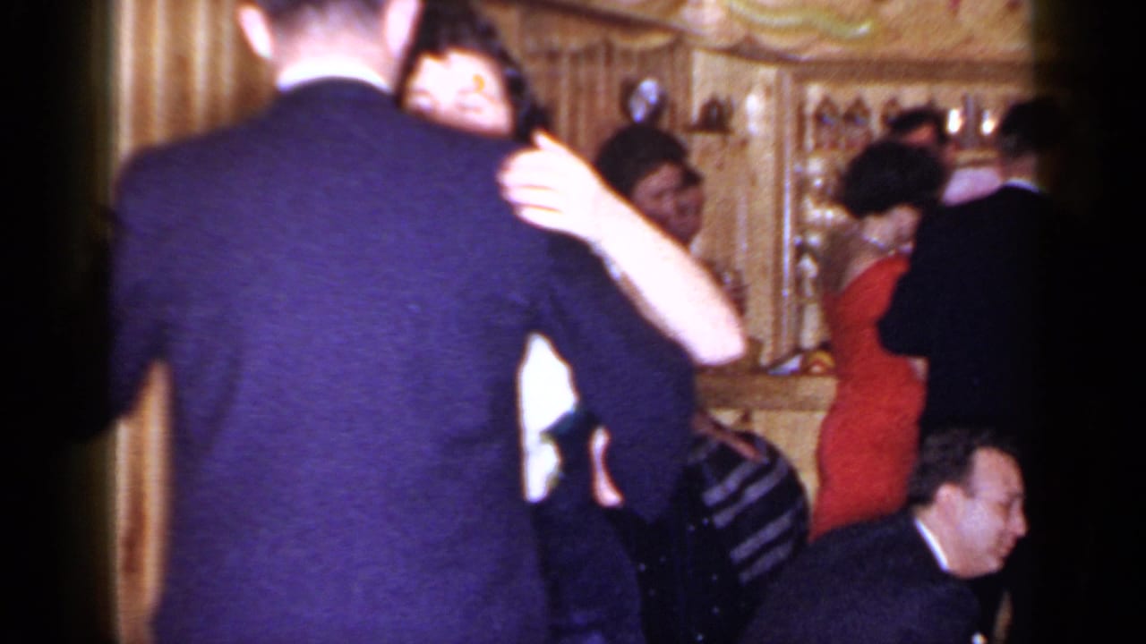 Couple dancing closely in a dim bar while other adults gather nearby.