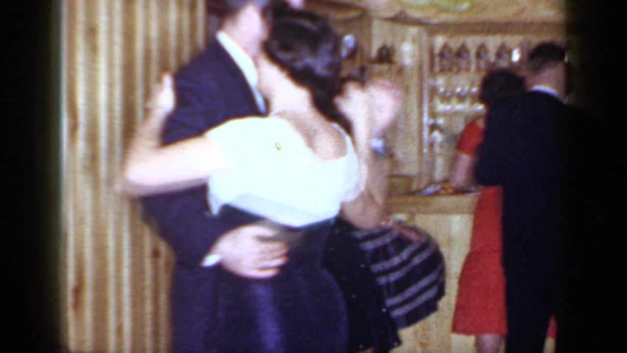 A couple dances closely in front of a bar while other guests stand nearby.