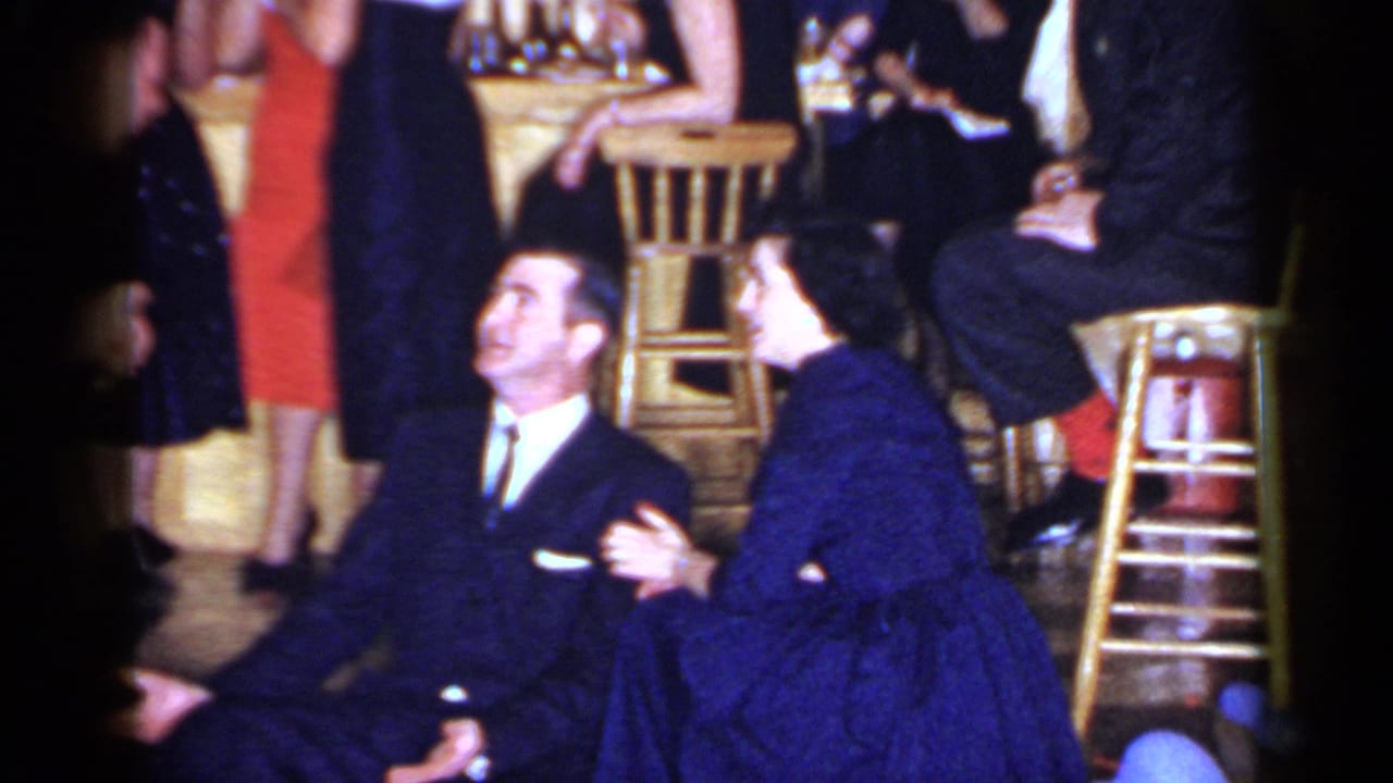In 1966 Mineola home-movie footage, a suited man sits beside a woman in a blue dress amid stools and guests on a dance floor.
