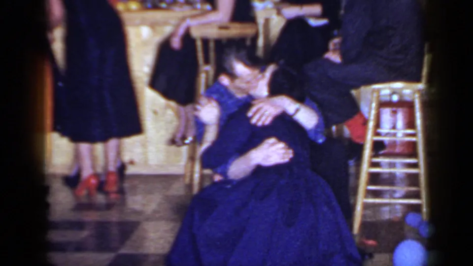 At the formal Mineola gathering, the suited man bends toward the woman in a blue dress as they embrace near stools and balloons.