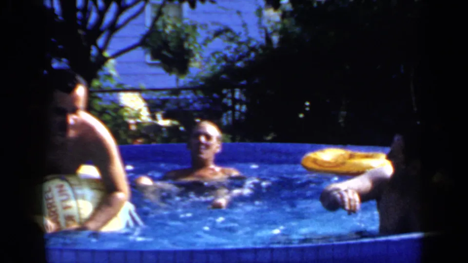 Three adult men are visible in the blue backyard pool, including one at the side with a yellow inflatable ring, in 1966 Mineola footage.