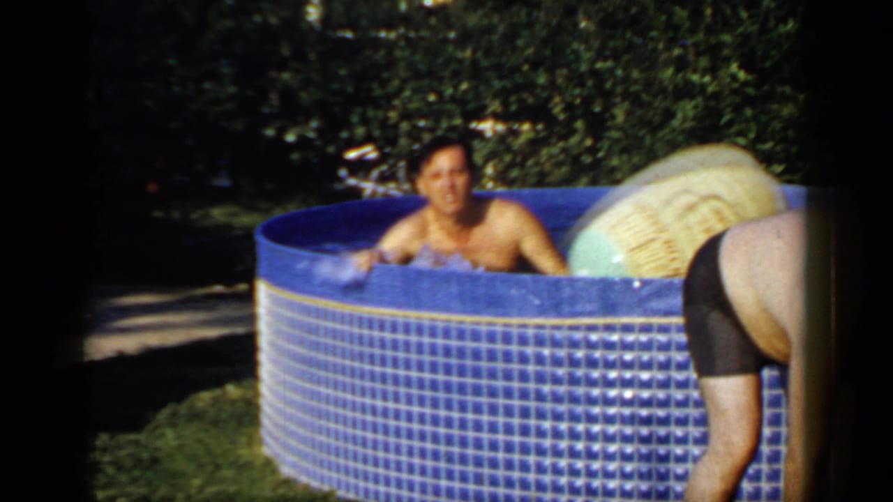 In 1966 Mineola home-movie footage, an adult man sits in a blue backyard pool while another adult bends beside a large beach ball.