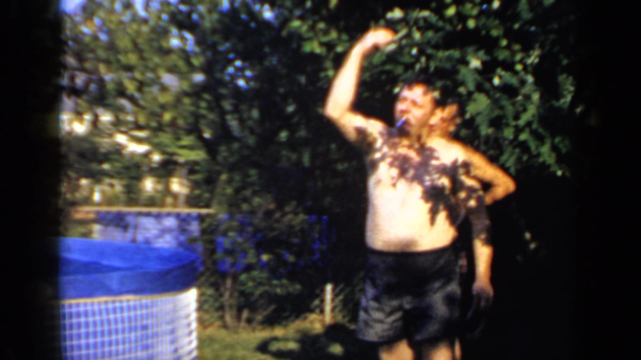 Shirtless man in dark swim trunks raises one arm near a blue backyard pool.