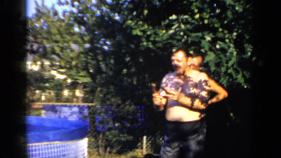 Two men stand close together near the blue pool during a 1966 Mineola backyard horseshoe moment on 8mm film.