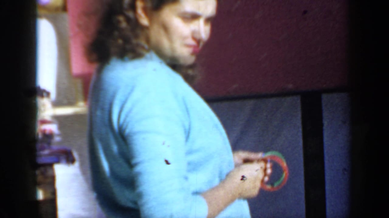 Woman in a light blue blouse stands beside a red exterior wall holding a small round object.