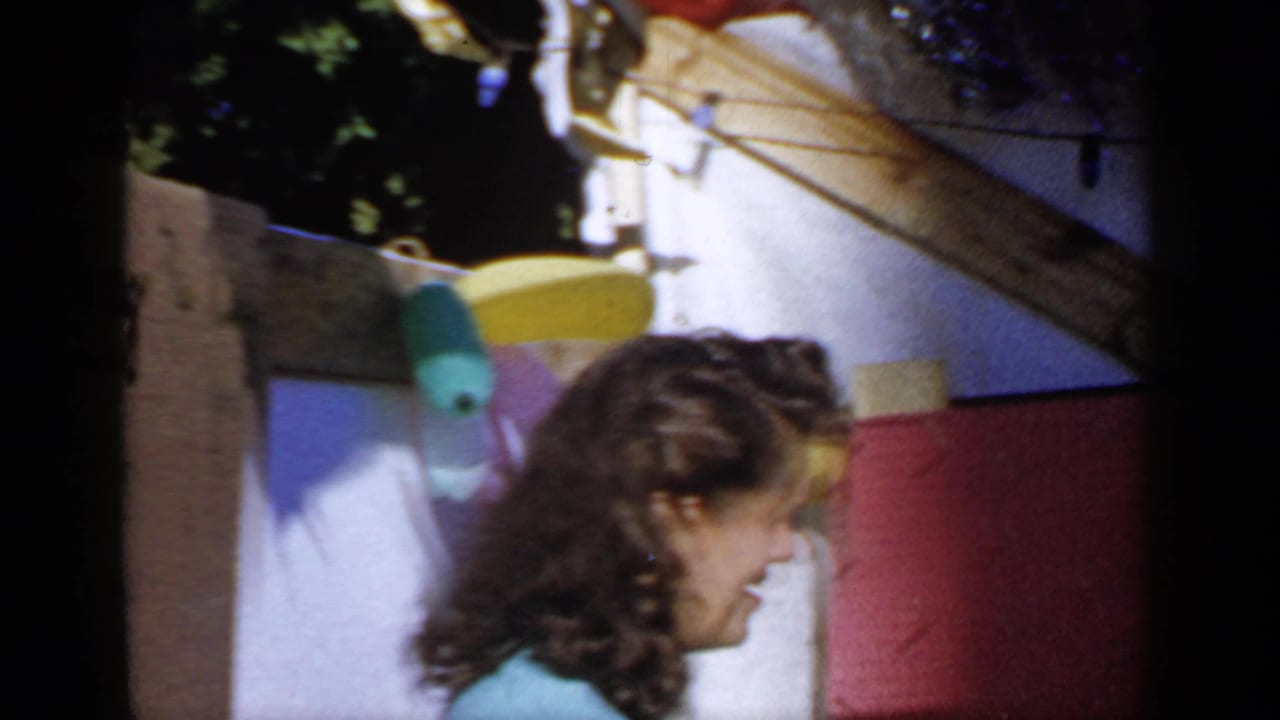 Woman in a light blue top smiles near outdoor paper decorations and a wooden structure.