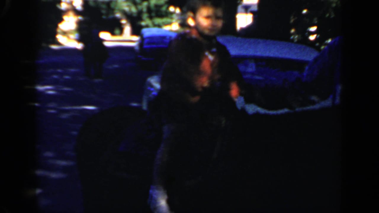 People near parked cars and a bright outdoor event area, partly obscured by dark film frame edges.