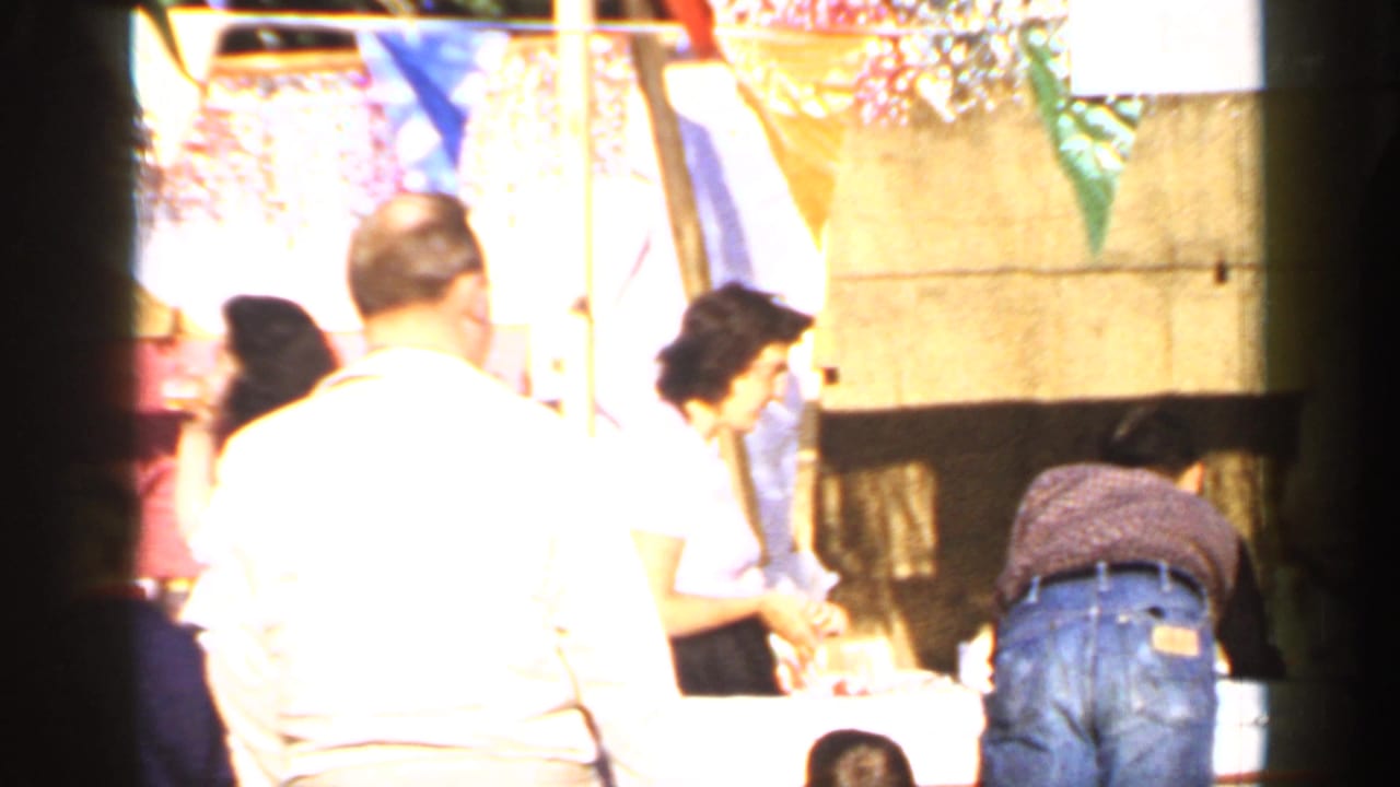 Adults at a Mineola community event table or booth in 1966, with colorful bunting and strong daylight exposure.