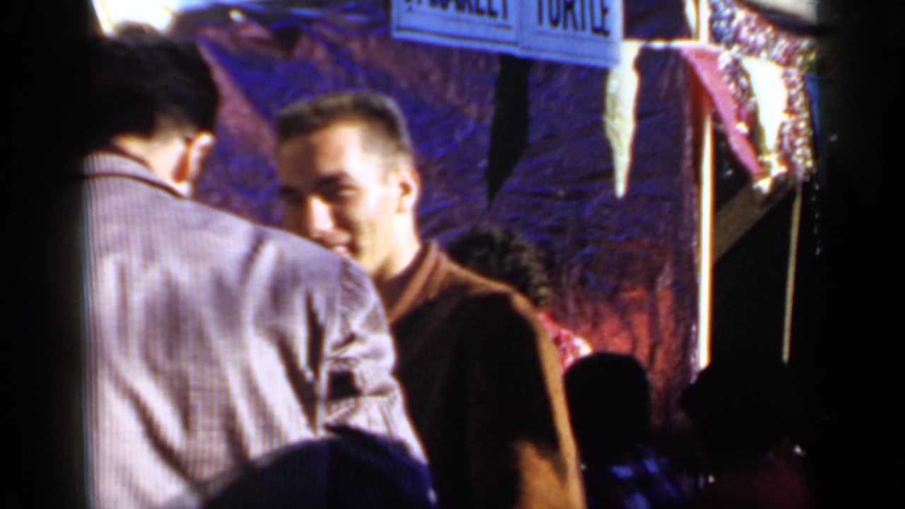 Young men standing near a parade stall or street-side structure with partial signage above.