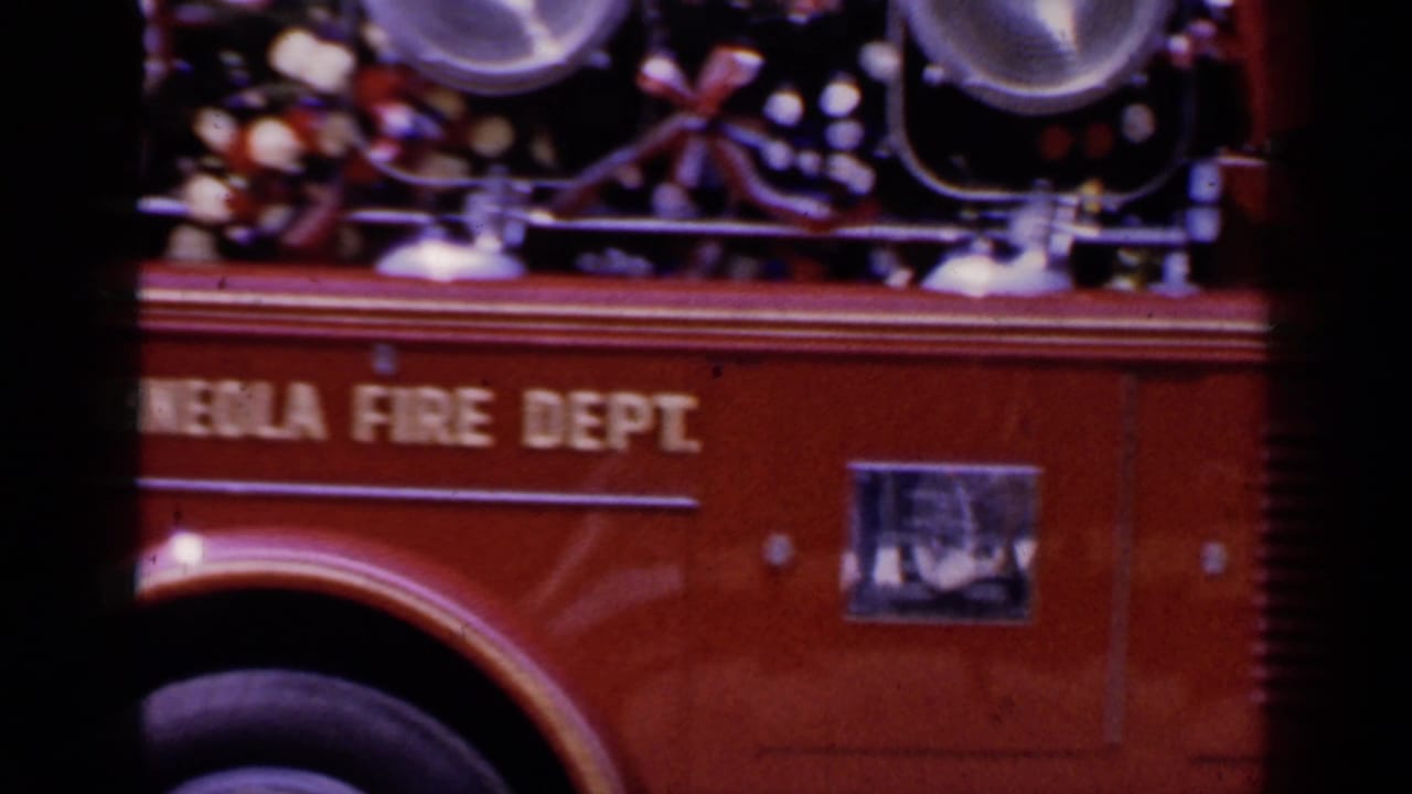 Close side view of a red fire truck with Mineola Fire Dept lettering and mounted equipment.
