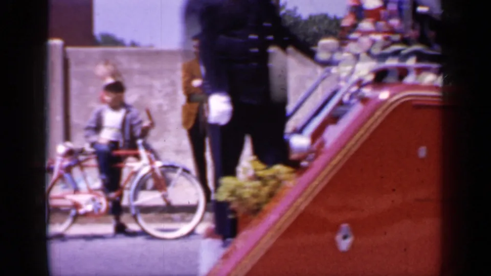 Sidewalk view in Mineola showing a young spectator with a bicycle beside the passing red fire department vehicle.
