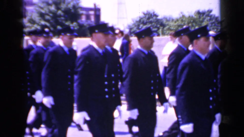 Cadets in dark formal uniforms and white gloves move past the camera in profile in Mineola, New York.
