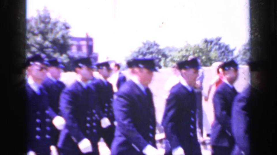 Additional cadets in dark uniforms continue the street procession in bright 1966 Mineola home-movie footage.