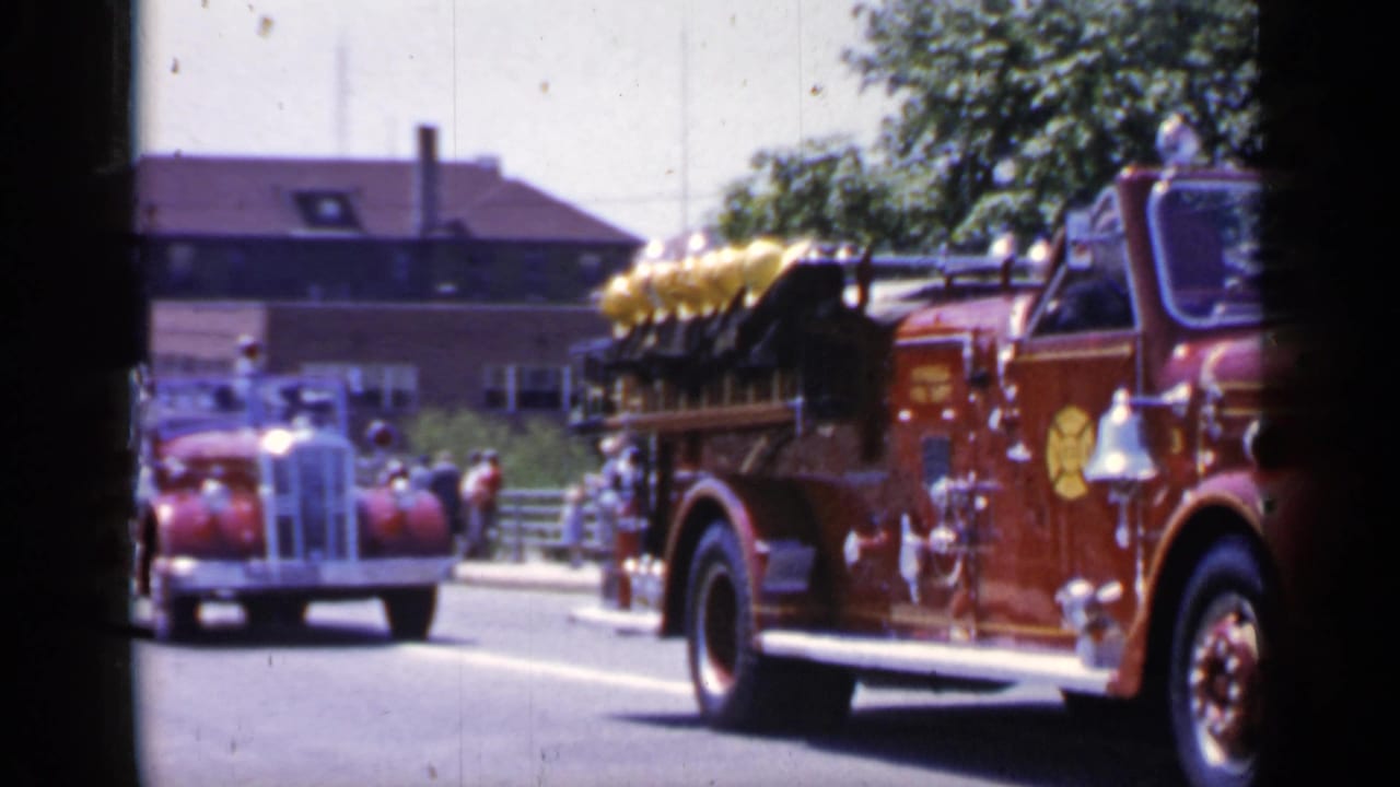 Fire engine moving out of frame while a red vintage car follows along the street.