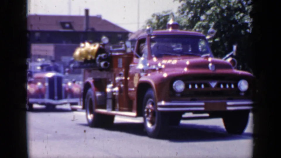 The red rescue truck fills the frame as it passes, showing side-mounted equipment and the soft color and grain of 8mm home-movie film.