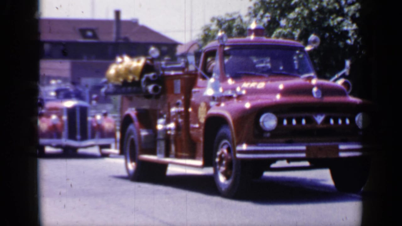 Red fire truck driving along a sunny street during a parade.