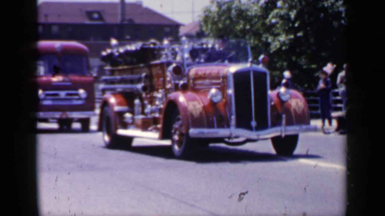 Antique red fire engine approaching with another red truck behind it.