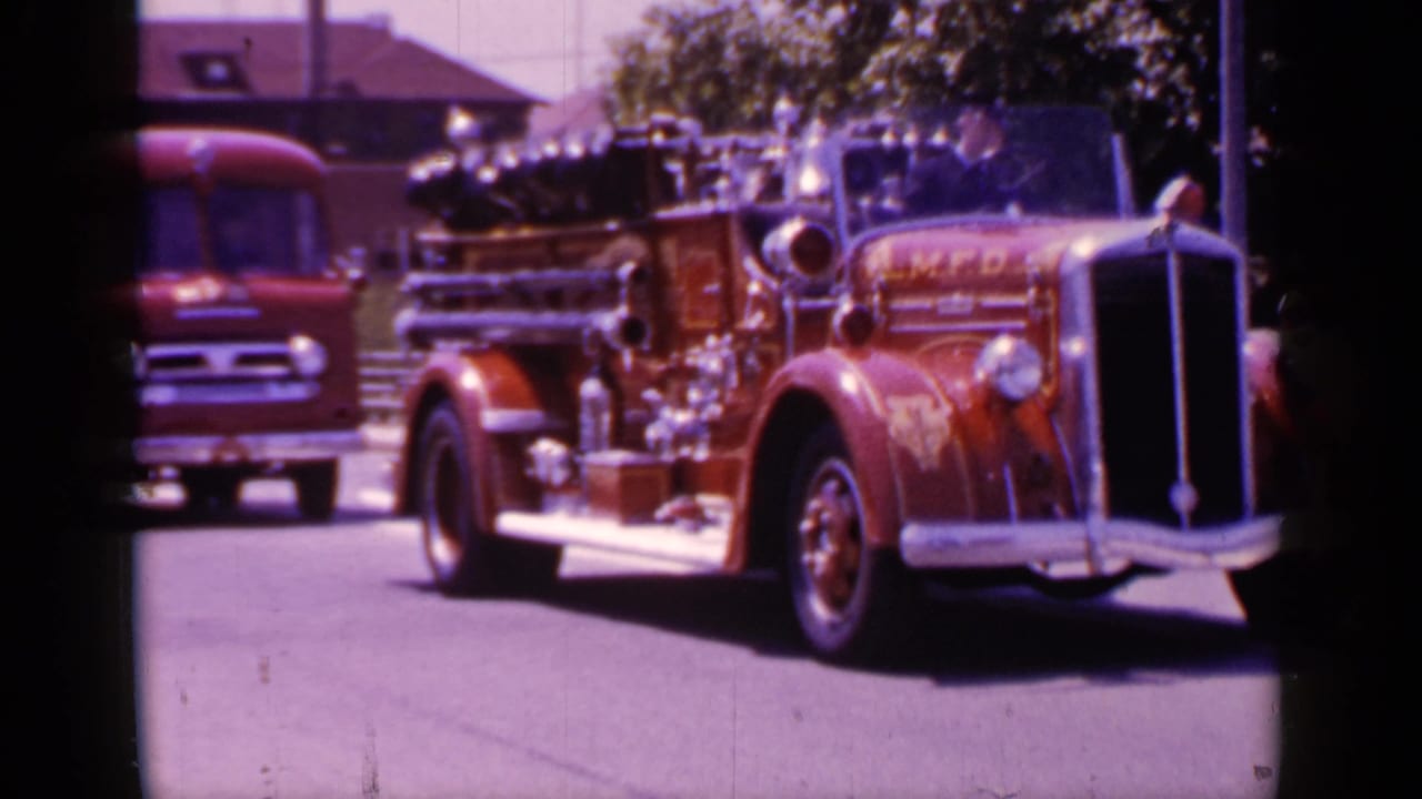 Red fire engine passes closer to the camera with chrome trim and department lettering visible.